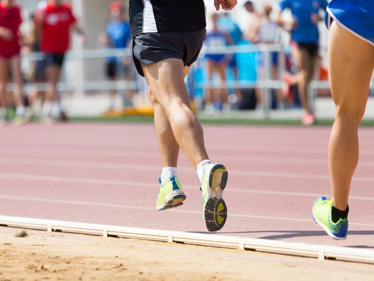 Zwei Läufer in Sportschuhen, die auf einer Laufbahn sprinten; Zuschauer im Hintergrund.