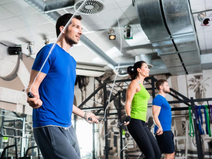 Drei Personen beim Seilspringen in einem modernen Fitnessstudio mit Geräten im Hintergrund.