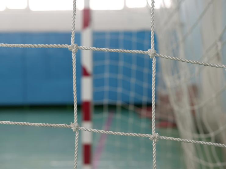 Nahaufnahme eines Handballtors mit weißem Netz und roten Markierungen auf der Wand in einer Sporthalle.